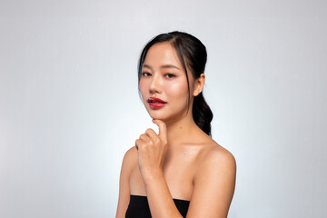 A beautiful Asian woman with perfect makeup and tanned skin poses against a grey studio background.