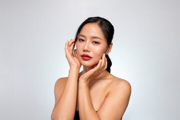 A young Asian woman with a perfect, beautiful face poses against a grey background, touches her face