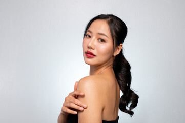 Obraz premium A gorgeous Asian model touches her glowing tanned skin while posing against a grey studio background
