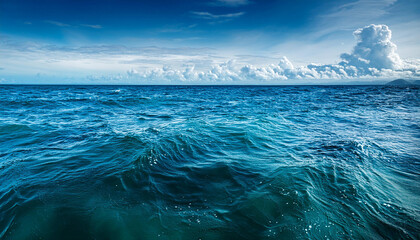 Deep blue ocean waves with distant horizon, under a slightly cloudy sky, shown in vivid daylight.