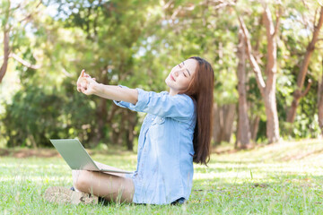Young woman who works in the park on a laptop. asia woman stretches after sitting for a long time. © tonjung