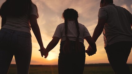 a family of three walks in the park at sunset. happy family kid dream concept. mom dad and daughter have a great time together. friendly lifestyle walk in a beautiful place at sunset