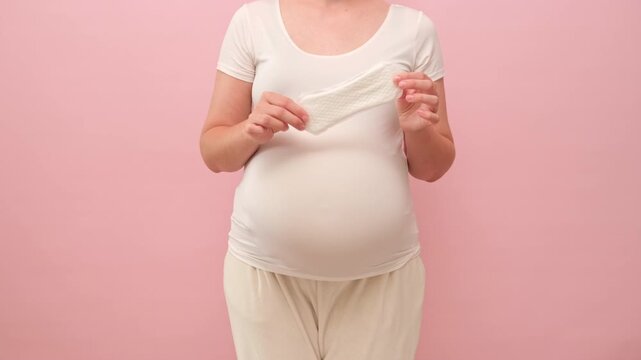 A pregnant woman holds a sanitary pad in her hands on a studio pink background