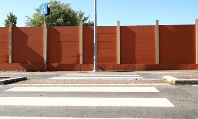 Metallic pole on sidewalk with brown precast concrete block wall on behind. Crosswalk, and street...