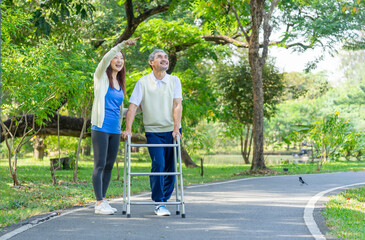 happy asian family walking in the park,adult daughter support her disabled senior father practice walking with walker,a young woman pointing to something both of them enjoy relaxing in nature