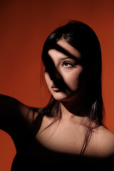 Brunette girl posing in a beam of light in the studio, on a red background, light and darkness.