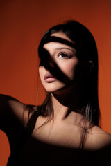 Brunette girl posing in a beam of light in the studio, on a red background, light and darkness.