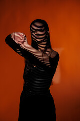 Brunette girl posing in a beam of light in the studio, on a red background, light and darkness.