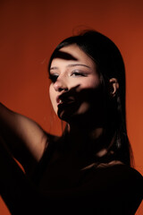 Brunette girl posing in a beam of light in the studio, on a red background, light and darkness.