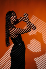 Brunette girl posing in a beam of light in the studio, on a red background, light and darkness.