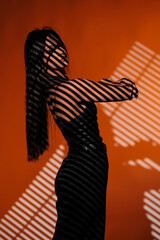 Brunette girl posing in a beam of light in the studio, on a red background, light and darkness.