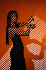 Brunette girl posing in a beam of light in the studio, on a red background, light and darkness.