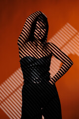 Brunette girl posing in a beam of light in the studio, on a red background, light and darkness.