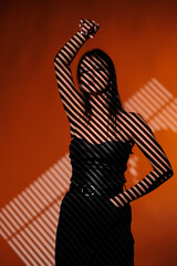 Brunette girl posing in a beam of light in the studio, on a red background, light and darkness.
