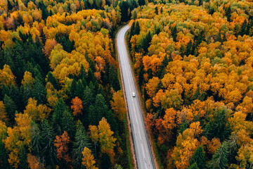 Aerial view of asphalt road with white car and colorful fall autumn forest in rural Finland.