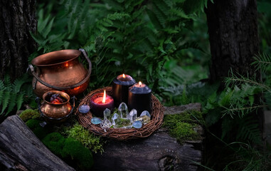 witch cauldrons, candles, amulet and quartz crystals on stump in forest, dark natural background....