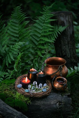 witch cauldrons, candles, amulet and quartz crystals on stump in forest, dark natural background....