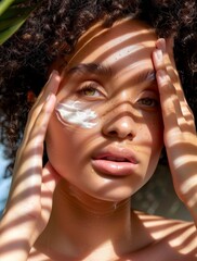 A young woman gently applies moisturizer to her face, illuminated by soft sunlight filtered through leafy shadows.