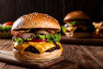 Close-up of a gourmet cheeseburger with bacon, lettuce, tomato, onion, and melted cheese on a sesame bun, placed on a wooden board with another burger in the background, on a rustic wooden table