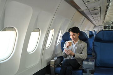Millennial businessman drinking coffee and using his mobile phone in an airplane