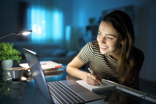 Happy woman using laptop in the night and taking notes
