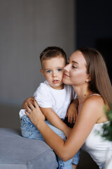 Young woman cuddling talking to small kid son, having fun together on couch in studio living room.