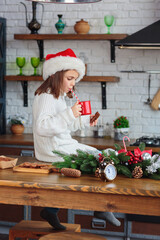 Kid sitting in a Christmas decorated cozy kitchen and wearing red santa claus hat