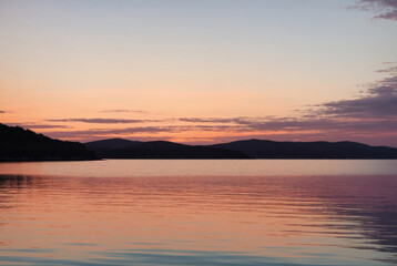 Fototapeta premium Clear blue sky sunset with glowing pink and purple horizon on calm ocean seascape background. Water surface texture. Picturesque dreamlike seascape, clouds-cape, nature. Panoramic view