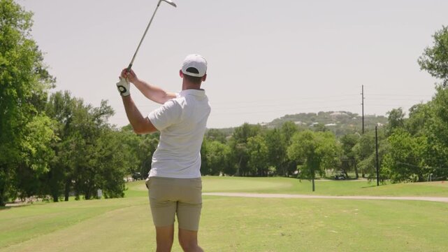 Male golfer hits wedge shot on par 3 golf course during middle of sunny summer day, golf swing in 4k slow motion