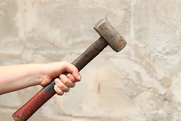 Sledgehammer in female hands on a blurred background. Close-up of a two-handed heavy hammer. Hand...