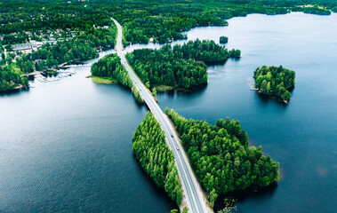 Aerial view of bridge asphalt road with cars and blue water lake or sea and green woods in Finland.