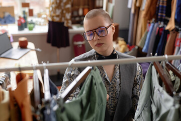 Portrait shot through clothing rack of fashionable female customer in vintage outfit and trendy...