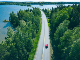 Aerial view of road with cars in green woods by blue lakes sea water in Finland