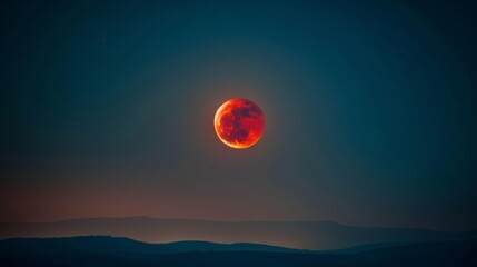 Obraz premium A stunning image of a red moon casting an ethereal glow over the dark, rolling hills below.