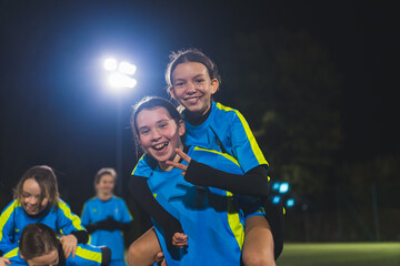 cheerful football player girl carrying her teammate with her back, girls soccer team celebrating victory. High quality photo