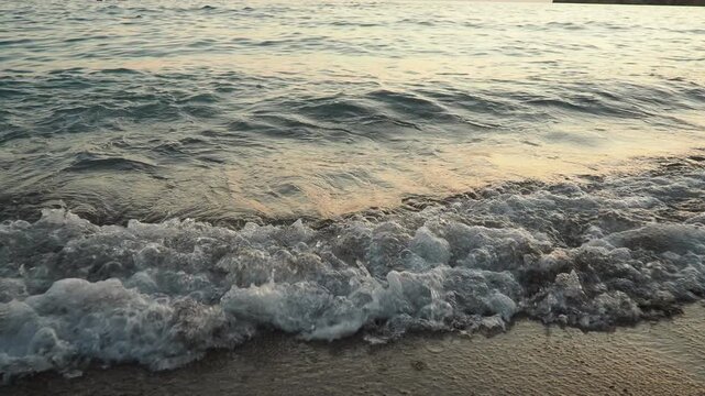 Waves gently lap at shore during stunning sunset over ocean. Golden sunlight reflects off waves as they roll onto shore, creating tranquil atmosphere at sunset by sea. Montenegro summer Canj
