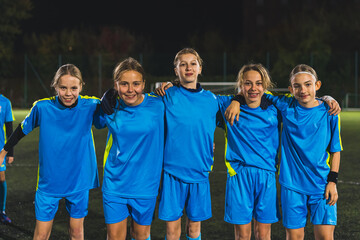 young girls with unifroms cuddling and posing together at the football practice in a stadium. High quality photo