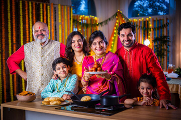 Indian family in traditional wear cooking food for diwali festival celebration at home - group photo