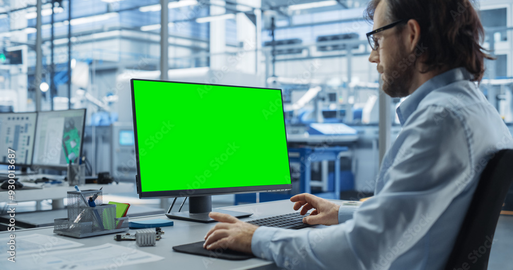 Fototapete Robotics Engineer Working on a Desktop Computer with Green Screen Chromakey Mock Up Display in a Startup Factory. High Tech Technological Research and Development Company with Autonomous Assembly Line