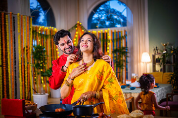 Indian young husband surprises wife with gift while cooking food on diwali festival eve in kitchen