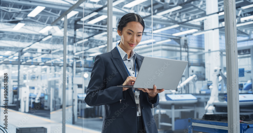 Poster asian factory manager working on laptop at futuristic industrial manufacture with autonomous robotic