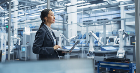 Beautiful Asian Female Engineer Standing Next to a Window in Office, Using Laptop Computer at an...