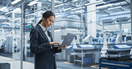 Beautiful Asian Female Engineer Standing Next to a Window in Office, Using Laptop Computer at...