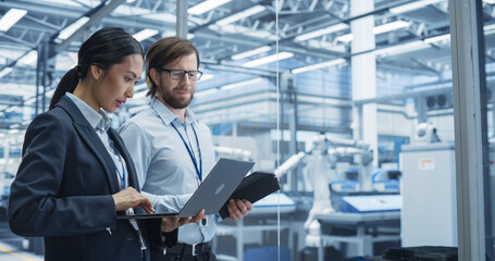 Two Multiethnic Engineers Standing in Office, Using Laptop and Tablet Computers at an Electronics...