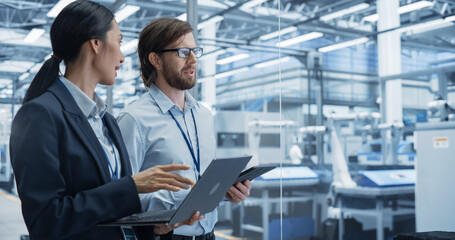 Naklejka premium Portrait of an Experienced Male and Female Engineers Standing in Agency Room, Using Computer Devices and Discussing Production at a Modern Automated Electronics Manufacture with Robot Arms