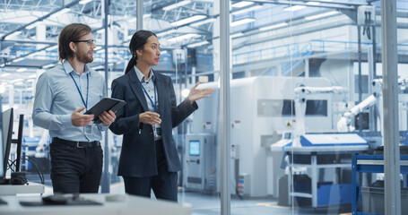 Two Diverse Engineers Walking in Office, Using Tablet Computer at an Electronics Factory. Female...