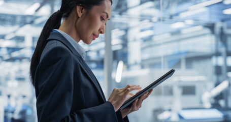 Beautiful Asian Female Engineer Standing Next to a Window in Office, Using Tablet Computer at an Electronics Manufacture. Specialist Using an Online Software to Program Robots on Assembly Line