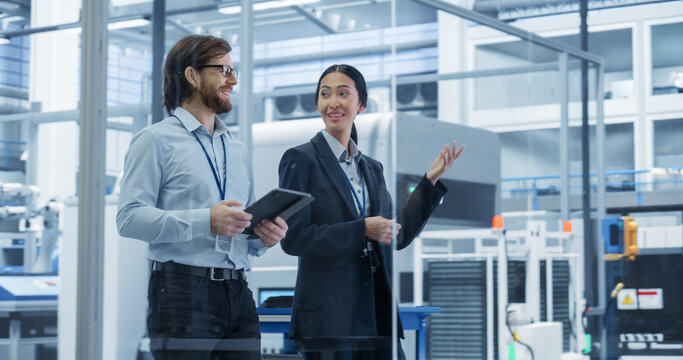 Portrait of an Experienced Male and Female Engineers Walking in Agency Room, Using Computer Tablet Device and Discussing Production at a Modern Automated Electronics Manufacture with Robotic Arms