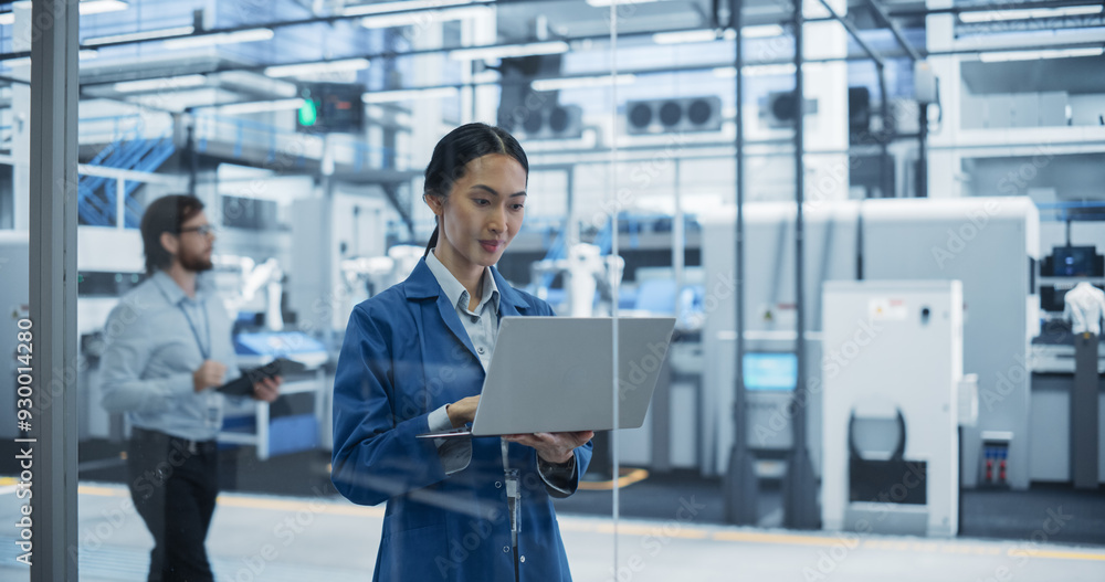 Poster electronics manufacturing technician in a blue coat working on a laptop computer at an assembly plan
