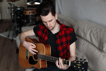 Obraz premium A man sits on a sofa and practices playing the guitar. Music and Hobbies